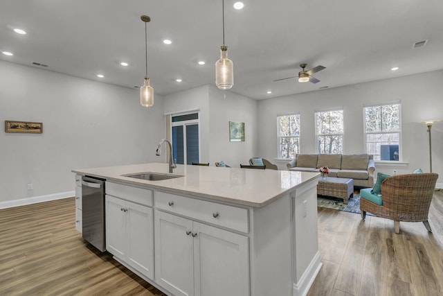 kitchen with sink, light hardwood / wood-style flooring, white cabinetry, hanging light fixtures, and a center island with sink