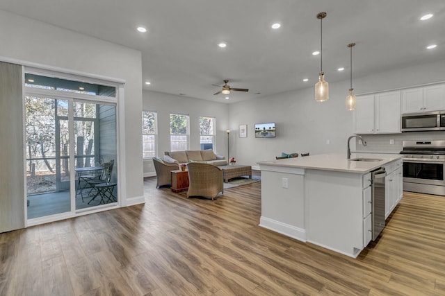 kitchen with sink, decorative light fixtures, a center island with sink, stainless steel appliances, and white cabinets