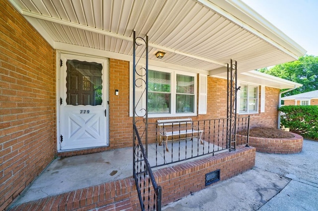 view of exterior entry with a porch and brick siding