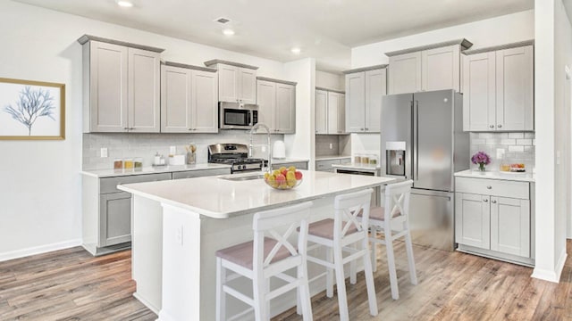 kitchen with backsplash, stainless steel appliances, light hardwood / wood-style floors, and gray cabinetry