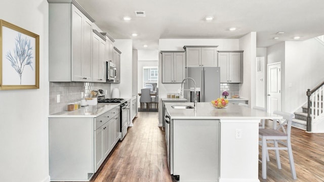 kitchen featuring gray cabinetry, a kitchen island with sink, appliances with stainless steel finishes, tasteful backsplash, and wood-type flooring