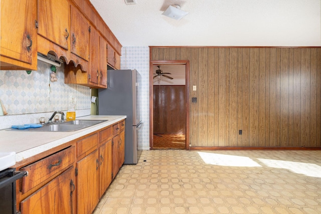 kitchen featuring sink, wood walls, tasteful backsplash, stainless steel fridge, and stove