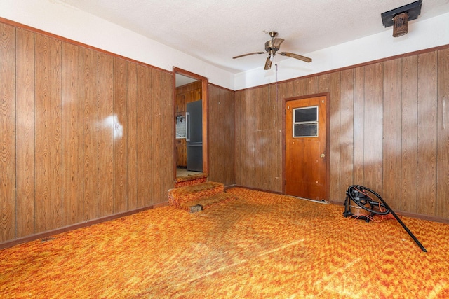 carpeted spare room featuring ceiling fan, a textured ceiling, and wood walls