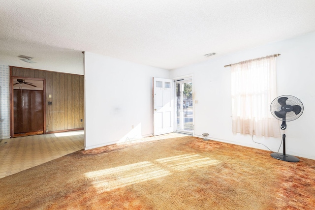 unfurnished room with wooden walls, carpet floors, and a textured ceiling