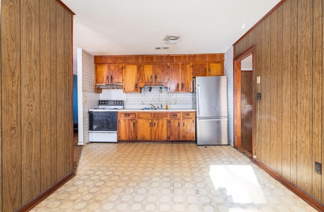 kitchen with wooden walls, sink, stainless steel refrigerator, and electric stove