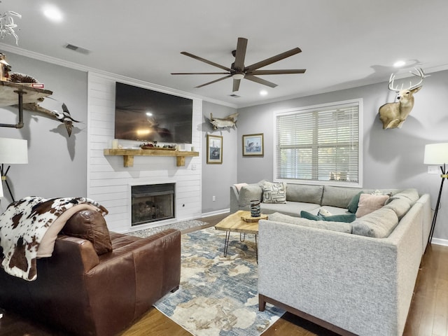 living room with dark wood-type flooring, ornamental molding, a large fireplace, and ceiling fan