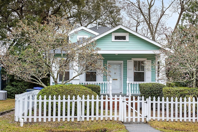 shotgun-style home featuring covered porch, a fenced front yard, cooling unit, and a gate