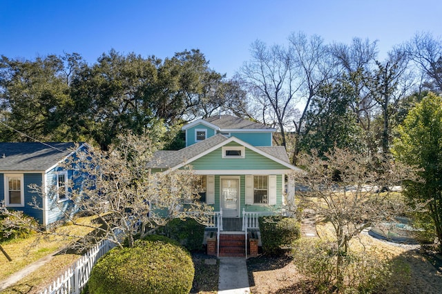view of front of house with a porch, roof with shingles, and fence