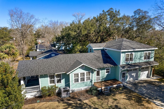 view of front facade featuring a porch, concrete driveway, an attached garage, a shingled roof, and ac unit