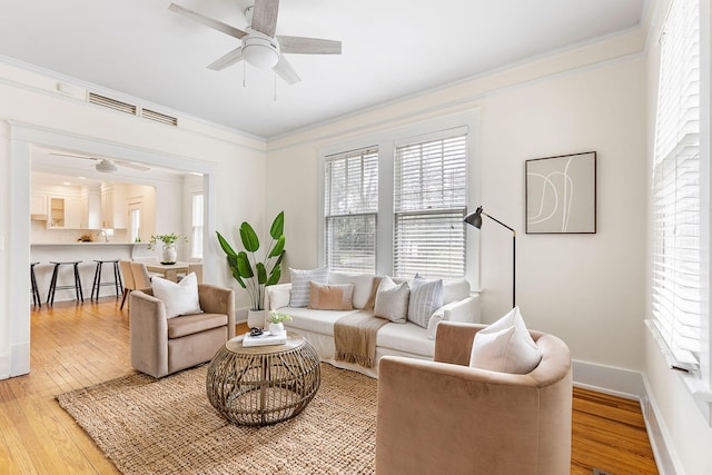 living area with ceiling fan, healthy amount of natural light, crown molding, light wood finished floors, and baseboards