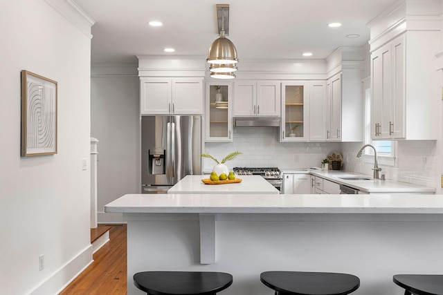 kitchen featuring stainless steel appliances, a sink, under cabinet range hood, a kitchen breakfast bar, and white cabinets