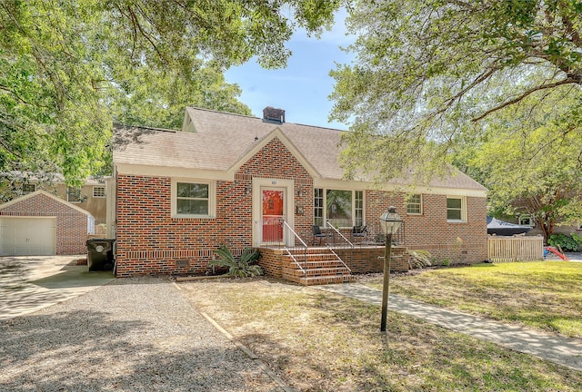 view of front facade featuring brick siding, driveway, a chimney, and a detached garage