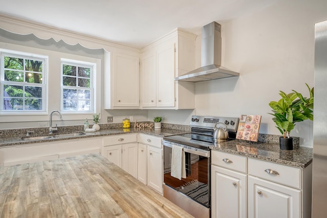 kitchen featuring wall chimney range hood, stainless steel electric range, a sink, and dark stone countertops