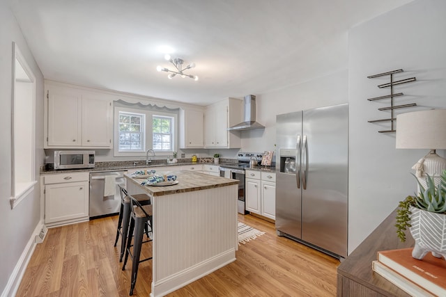 kitchen with white cabinets, light wood-style flooring, stainless steel appliances, and wall chimney exhaust hood