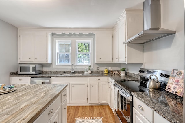 kitchen with light wood-type flooring, a sink, white cabinets, stainless steel appliances, and wall chimney exhaust hood