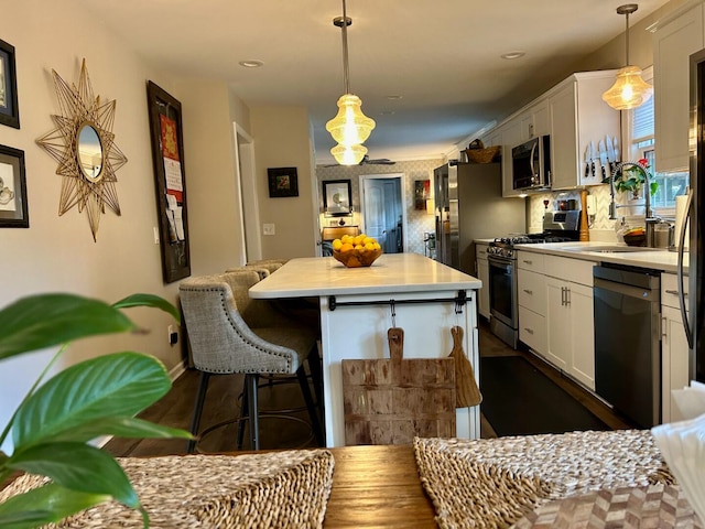 kitchen featuring sink, a kitchen island, hanging light fixtures, white cabinetry, and stainless steel appliances