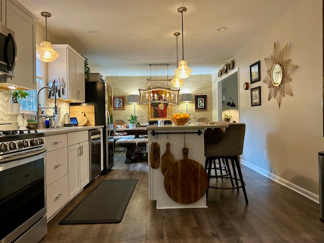 kitchen with appliances with stainless steel finishes, hanging light fixtures, dark hardwood / wood-style floors, and white cabinetry