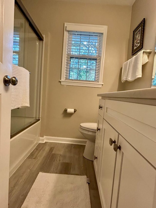 full bathroom with vanity, toilet, wood-type flooring, and shower / bath combination with glass door