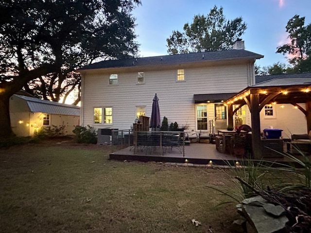 back house at dusk featuring a yard, a gazebo, a deck, and outdoor lounge area