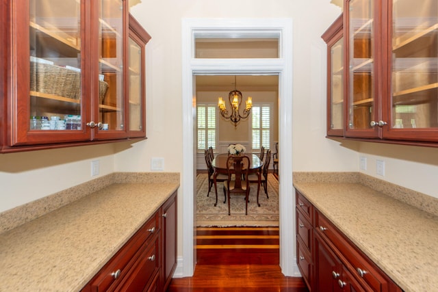 kitchen featuring dark wood-style floors, light stone counters, glass insert cabinets, and pendant lighting