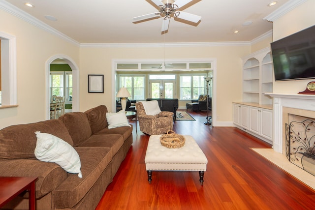 living area featuring dark wood-type flooring, arched walkways, ornamental molding, and a high end fireplace