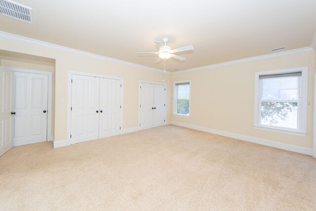 unfurnished bedroom with multiple closets, light colored carpet, visible vents, ornamental molding, and baseboards