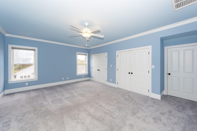 unfurnished bedroom with light carpet, ornamental molding, two closets, and ceiling fan