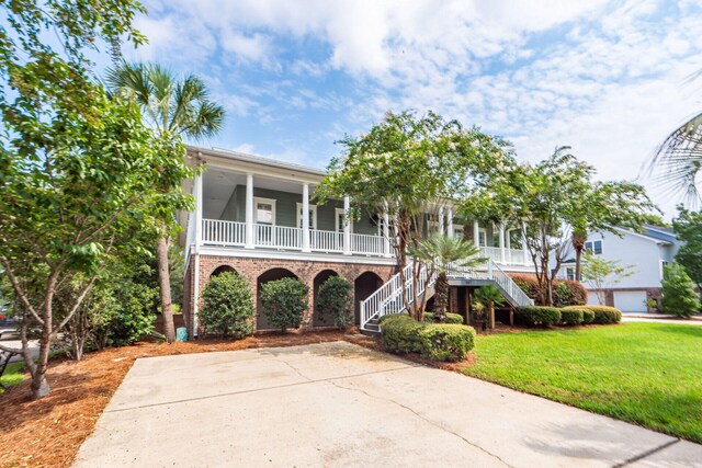 coastal home with covered porch, a front lawn, stairway, and brick siding