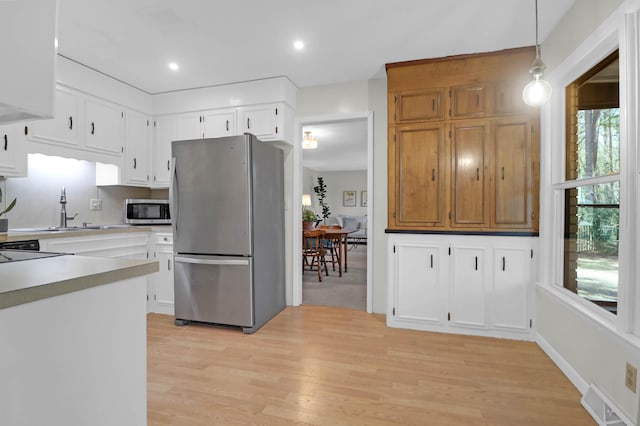 kitchen featuring visible vents, light wood-style flooring, stainless steel appliances, light countertops, and decorative light fixtures