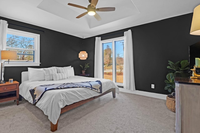 carpeted bedroom with a raised ceiling and ceiling fan