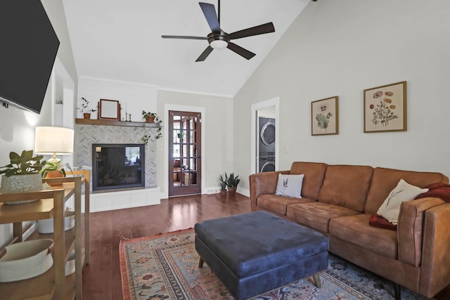 living area featuring wood finished floors, baseboards, ceiling fan, a tiled fireplace, and stacked washer / dryer