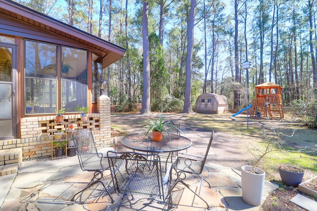 view of patio featuring a storage unit, outdoor dining area, an outdoor structure, and a playground