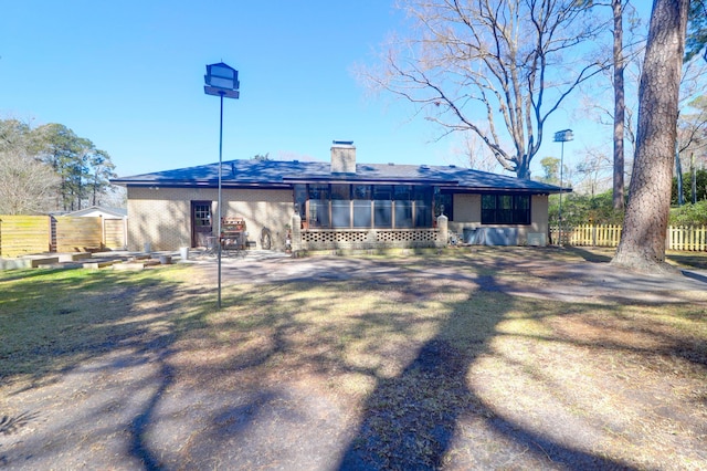 rear view of house featuring brick siding, a chimney, and fence