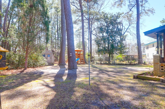 view of yard with playground community, an outdoor structure, a shed, and fence