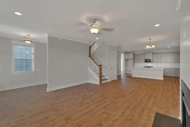 unfurnished living room featuring ceiling fan with notable chandelier and light hardwood / wood-style flooring