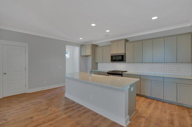 kitchen featuring appliances with stainless steel finishes, an island with sink, backsplash, light wood-type flooring, and ornamental molding