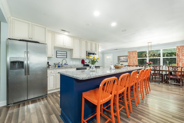 kitchen with light stone counters, dark hardwood / wood-style floors, stainless steel appliances, sink, and a center island