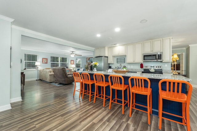 kitchen featuring appliances with stainless steel finishes, crown molding, dark wood-type flooring, and a breakfast bar area