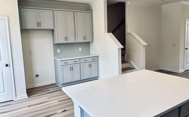 kitchen featuring tasteful backsplash, crown molding, gray cabinets, and light hardwood / wood-style flooring