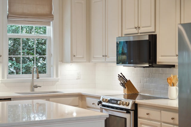 kitchen with tasteful backsplash, sink, white cabinets, and appliances with stainless steel finishes