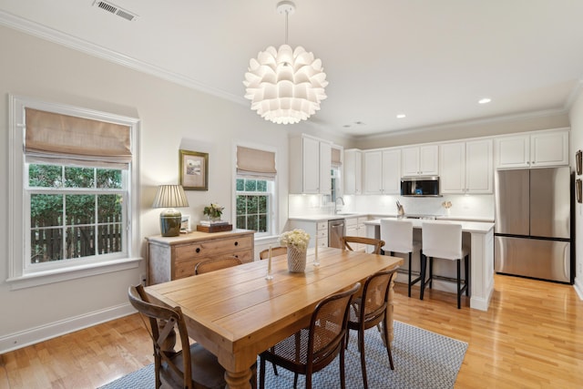 dining space with ornamental molding, sink, a notable chandelier, and light hardwood / wood-style floors