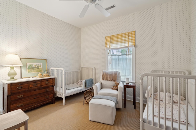 carpeted bedroom with ceiling fan and a crib