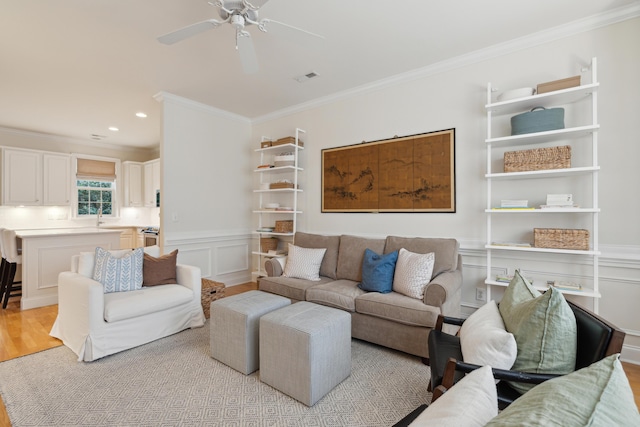 living room featuring ornamental molding, ceiling fan, and light wood-type flooring