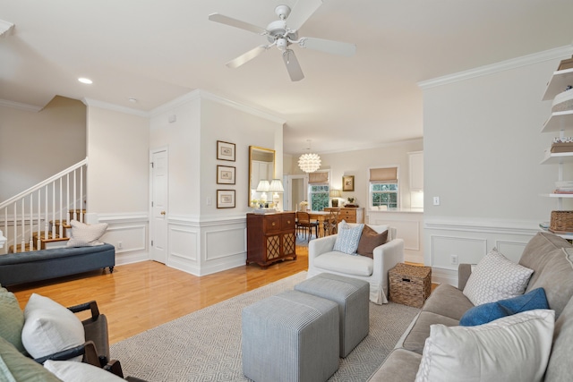 living room with crown molding, ceiling fan with notable chandelier, and light wood-type flooring