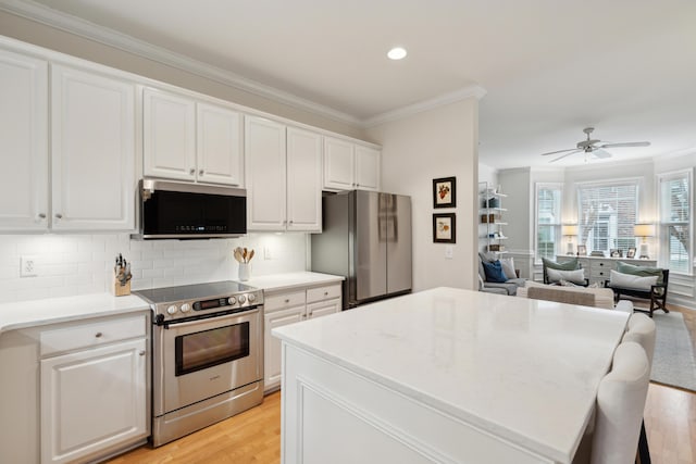 kitchen with appliances with stainless steel finishes, white cabinetry, ornamental molding, a kitchen island, and decorative backsplash