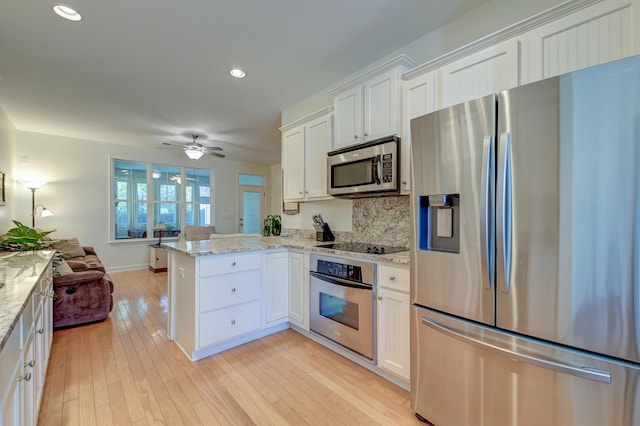 kitchen featuring appliances with stainless steel finishes, open floor plan, a peninsula, light stone countertops, and white cabinetry