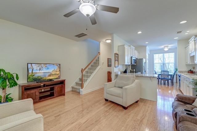 living room with stairway, ceiling fan, visible vents, and light wood-style floors