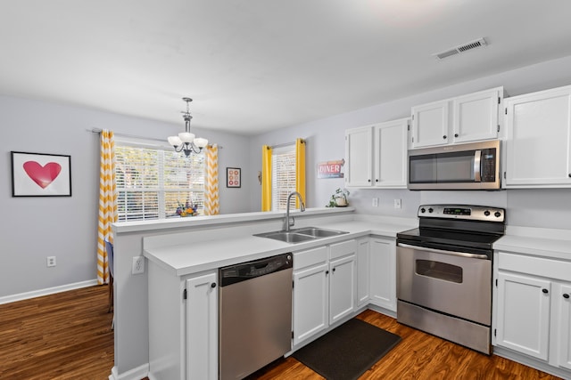 kitchen with stainless steel appliances, a peninsula, dark wood-style flooring, a sink, and visible vents