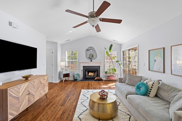 living area featuring a warm lit fireplace, a ceiling fan, vaulted ceiling, and wood finished floors