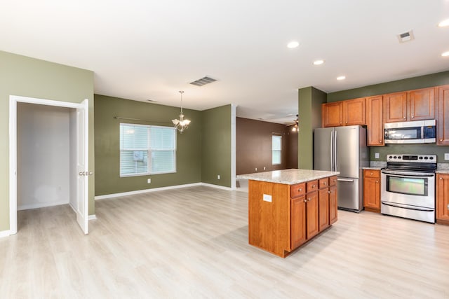 kitchen with a kitchen island, appliances with stainless steel finishes, pendant lighting, light stone countertops, and light wood-type flooring